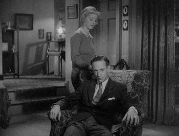Movie still from “Of Human Bondage” (1934), directed by John Cromwell – A man sitting in a chair with a woman standing next to him; Medium shot, High angle