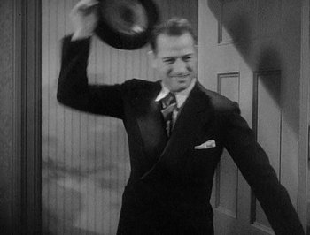 Movie still from “Of Human Bondage” (1934), directed by John Cromwell – A black and white photo of a man in a suit and tie holding a hat; Medium shot, Over the shoulder angle