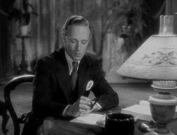 Movie still from “Of Human Bondage” (1934), directed by John Cromwell – A man in a suit and tie writing on a piece of paper; Medium shot, High angle