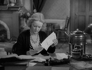 Movie still from “Of Human Bondage” (1934), directed by John Cromwell – An older woman sitting at a table looking at a piece of paper; Medium shot, High angle