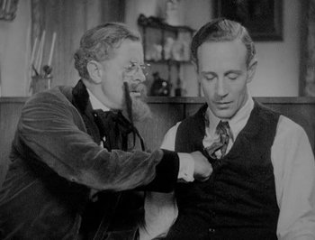 Movie still from “Of Human Bondage” (1934), directed by John Cromwell – An older man helping a younger man with a tie; Medium shot, Over the shoulder angle
