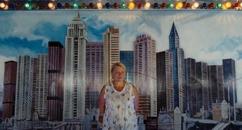 Movie still from “Paradise: Love” (2012), directed by Ulrich Seidl – A woman standing in front of a painting of a city skyline; Wide shot, Low angle