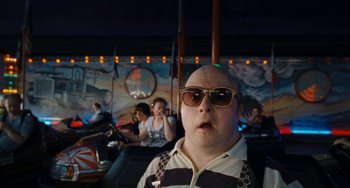 Movie still from “Paradise: Love” (2012), directed by Ulrich Seidl – A bald man wearing sunglasses and a striped shirt is in front of a crowd; Close Up shot, High angle