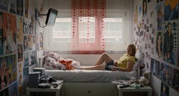 Movie still from “Paradise: Love” (2012), directed by Ulrich Seidl – A woman laying on a bed in front of a television; Wide shot, High angle