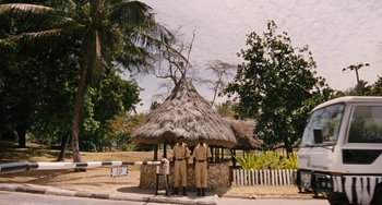Movie still from “Paradise: Love” (2012), directed by Ulrich Seidl – Two men standing in front of a thatched hut; Wide shot, Low angle