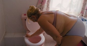 Movie still from “Paradise: Love” (2012), directed by Ulrich Seidl – A woman in a pink bra is putting something in a toilet; Medium shot, High angle