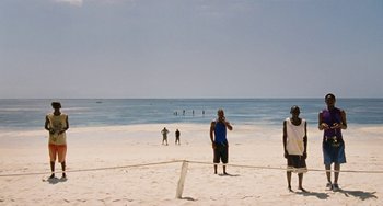 Movie still from “Paradise: Love” (2012), directed by Ulrich Seidl – A group of people standing on top of a sandy beach; Extreme Wide shot, Over the shoulder angle