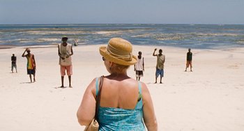 Movie still from “Paradise: Love” (2012), directed by Ulrich Seidl – A woman wearing a straw hat standing on a beach; Wide shot, High angle