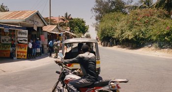 Movie still from “Paradise: Love” (2012), directed by Ulrich Seidl – A man on a motorcycle driving down a street; Extreme Wide shot, High angle