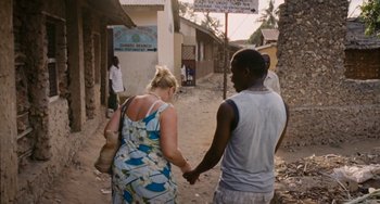 Movie still from “Paradise: Love” (2012), directed by Ulrich Seidl – A man and a woman holding hands while walking down a street; Wide shot, High angle