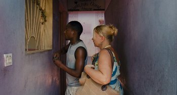 Movie still from “Paradise: Love” (2012), directed by Ulrich Seidl – A woman and a young man standing next to each other; Medium shot, Over the shoulder angle