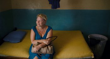Movie still from “Paradise: Love” (2012), directed by Ulrich Seidl – A woman sitting on a couch holding a purse; Medium shot, High angle