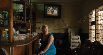 Movie still from “Paradise: Love” (2012), directed by Ulrich Seidl – A woman sitting at a table in front of a television; Wide shot, Over the shoulder angle