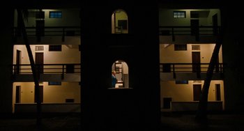 Movie still from “Paradise: Love” (2012), directed by Ulrich Seidl – A person is sitting in a room in a dark room; Extreme Wide shot, Low angle