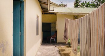 Movie still from “Paradise: Love” (2012), directed by Ulrich Seidl – A man sitting on a chair in front of a building; Wide shot, High angle