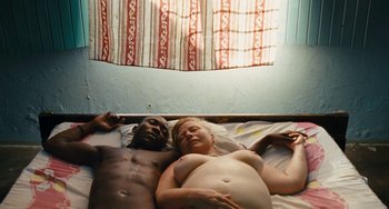 Movie still from “Paradise: Love” (2012), directed by Ulrich Seidl – A man and a woman laying in a bed together; Medium shot, Overhead angle