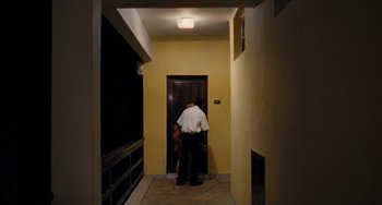 Movie still from “Paradise: Love” (2012), directed by Ulrich Seidl – A man standing in front of an open door in a hallway; Wide shot, Low angle