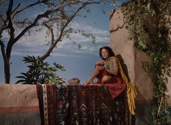 Movie still from “Samson and Delilah” (1949), directed by Cecil B. DeMille – A woman sitting on top of a rug near a tree; Wide shot, High angle