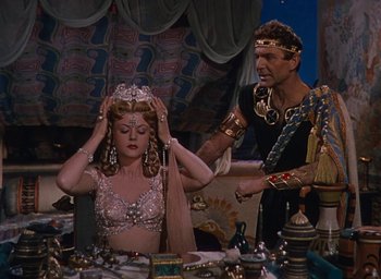 Movie still from “Samson and Delilah” (1949), directed by Cecil B. DeMille – A man and a woman in a costume in front of a table; Medium shot, Over the shoulder angle