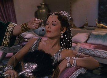 Movie still from “Samson and Delilah” (1949), directed by Cecil B. DeMille – A woman is sitting on a bed and is getting ready for a show; Medium shot, High angle