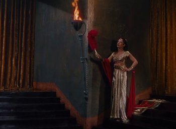 Movie still from “Samson and Delilah” (1949), directed by Cecil B. DeMille – A woman standing next to a staircase holding a red fan; Wide shot, High angle