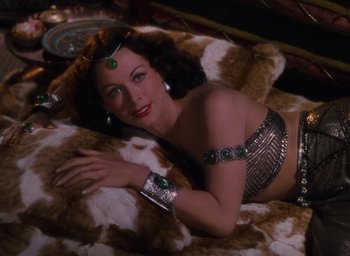 Movie still from “Samson and Delilah” (1949), directed by Cecil B. DeMille – A woman laying on top of a bed wearing jewelry; Medium shot, Overhead angle