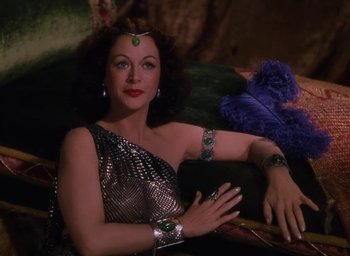 Movie still from “Samson and Delilah” (1949), directed by Cecil B. DeMille – A woman in a silver dress sitting next to a blue creature; Medium shot, High angle