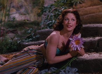Movie still from “Samson and Delilah” (1949), directed by Cecil B. DeMille – A beautiful woman laying on some steps holding a flower; Medium shot, High angle