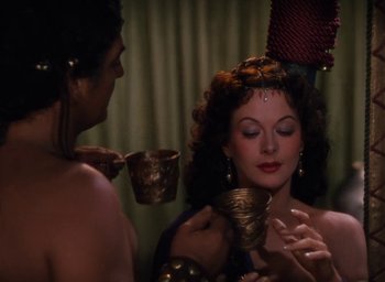 Movie still from “Samson and Delilah” (1949), directed by Cecil B. DeMille – A woman is holding a bowl while another woman looks on; Medium shot, Over the shoulder angle