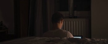 Movie still from “Simon Killer” (2012), directed by Antonio Campos – A man sitting on a bed looking at a computer screen; Medium shot, High angle