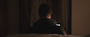 Movie still from “Simon Killer” (2012), directed by Antonio Campos – A man sitting in a chair looking at a cell phone; Medium shot, Low angle