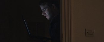Movie still from “Simon Killer” (2012), directed by Antonio Campos – A young man is looking at a computer screen in the dark; Close Up shot, Low angle