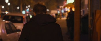 Movie still from “Simon Killer” (2012), directed by Antonio Campos – A person wearing a jacket is standing on a street; Medium shot, Over the shoulder angle
