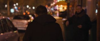 Movie still from “Simon Killer” (2012), directed by Antonio Campos – A man in a brown jacket standing in front of lights; Medium shot, Over the shoulder angle