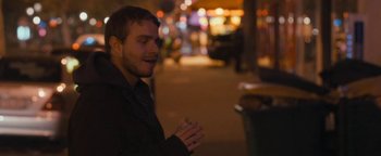 Movie still from “Simon Killer” (2012), directed by Antonio Campos – A man standing on the sidewalk holding a cigarette; Close Up shot, Over the shoulder angle
