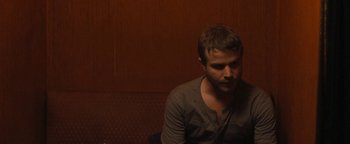 Movie still from “Simon Killer” (2012), directed by Antonio Campos – A man sitting in front of a wooden wall; Close Up shot, Over the shoulder angle