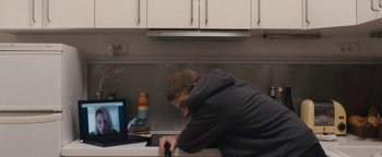 Movie still from “Simon Killer” (2012), directed by Antonio Campos – A young man working on a laptop in a kitchen; Medium shot, High angle