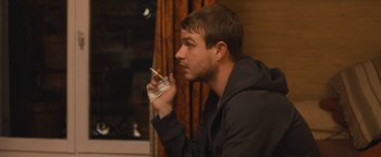 Movie still from “Simon Killer” (2012), directed by Antonio Campos – A man smoking a cigarette while sitting in a room; Close Up shot, Over the shoulder angle
