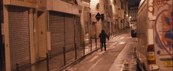 Movie still from “Simon Killer” (2012), directed by Antonio Campos – A person walking down a street at night near buildings; Extreme Wide shot, High angle
