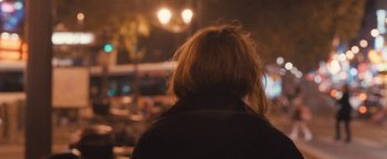 Movie still from “Simon Killer” (2012), directed by Antonio Campos – A woman with a blonde hair style is looking at a street light at night; Close Up shot, Over the shoulder angle