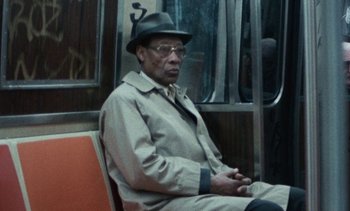 Movie still from “Smithereens” (1982), directed by Susan Seidelman – An older man sitting on a chair on a train; Medium shot, High angle