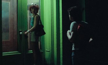 Movie still from “Smithereens” (1982), directed by Susan Seidelman – A woman standing next to a man in a green room; Medium shot, Over the shoulder angle