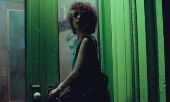Movie still from “Smithereens” (1982), directed by Susan Seidelman – A woman with red curly hair wearing sunglasses and holding a purse; Medium shot, Low angle