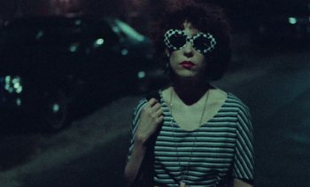Movie still from “Smithereens” (1982), directed by Susan Seidelman – A woman wearing sunglasses and a striped shirt; Medium shot, Over the shoulder angle