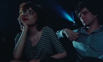 Movie still from “Smithereens” (1982), directed by Susan Seidelman – Two people sitting next to each other in a dark room; Medium shot, Over the shoulder angle