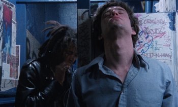Movie still from “Smithereens” (1982), directed by Susan Seidelman – A man with dreadlocks is leaning against a wall while another man with headphones looks at him; Close Up shot, Low angle