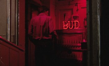Movie still from “Smithereens” (1982), directed by Susan Seidelman – A man standing next to a bar in a red room; Medium shot, Low angle