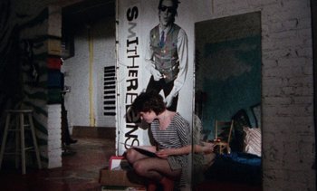 Movie still from “Smithereens” (1982), directed by Susan Seidelman – A woman sitting on the ground in front of a poster; Wide shot, High angle
