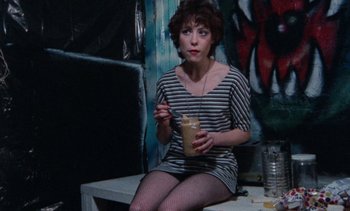 Movie still from “Smithereens” (1982), directed by Susan Seidelman – A woman sitting on top of a table holding a drink; Medium shot, High angle