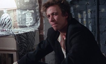 Movie still from “Smithereens” (1982), directed by Susan Seidelman – A man in a suit sitting in a room; Close Up shot, Low angle